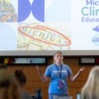 woman presenting in front of a projector screen that reads "Michigan Climate Education Hub"